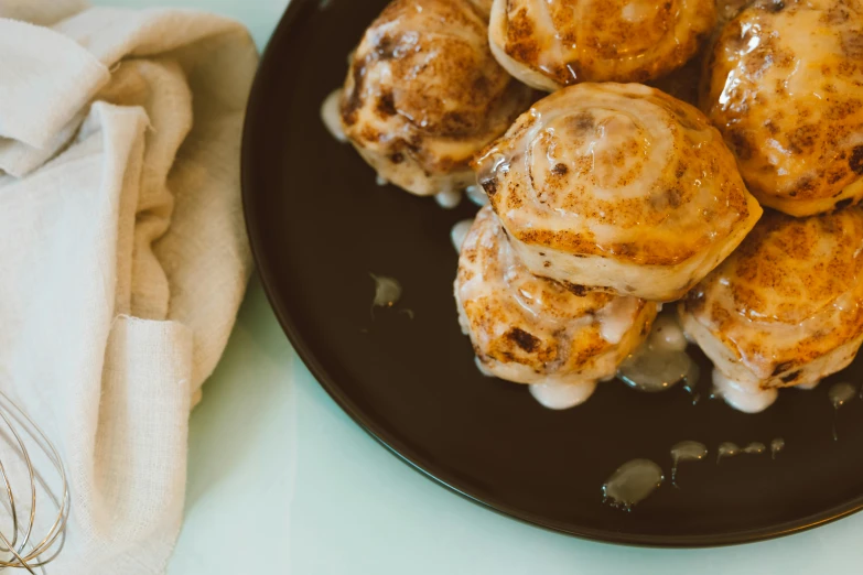 a black plate topped with cinnamon rolls covered in icing, unsplash, baroque, living food adorable pancake, background image, 3 4 5 3 1, dumplings on a plate