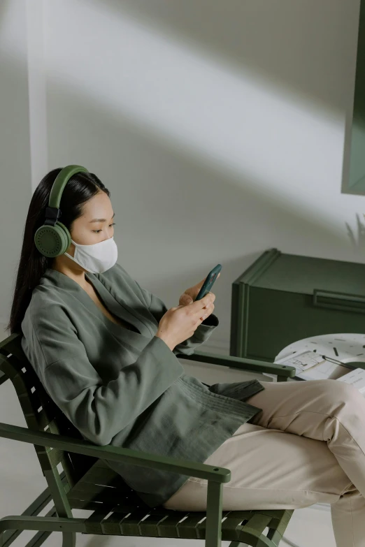 a woman sitting in a chair using a cell phone, by Jang Seung-eop, trending on pexels, happening, green facemask, wearing headphones, sitting on the edge of a bed, curated collections