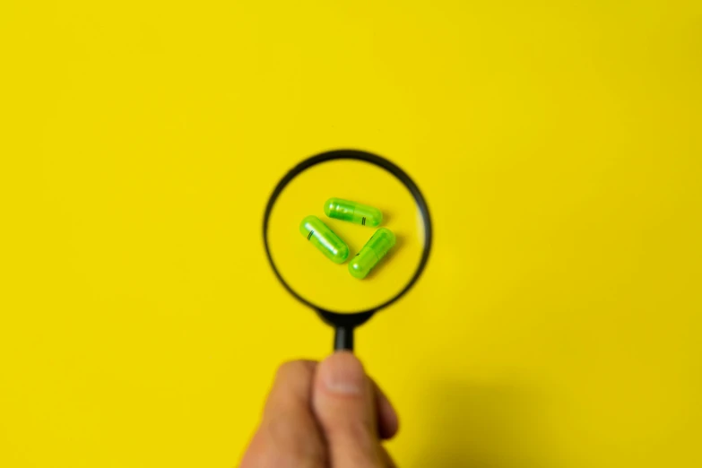 a close up of a person holding a magnifying glass, by Emma Andijewska, pexels, synthetism, pills, neon green, on yellow paper, gif