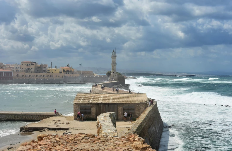 a group of people standing on top of a pier next to the ocean, pexels contest winner, graffiti, jerusalem, rough seas in background, preserved historical, light house