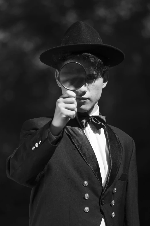 a man in a suit and hat holding a magnifying glass, a black and white photo, inspired by Jean Tabaud, pexels contest winner, robert sheehan, victorian style costume, female spy, declan mckenna