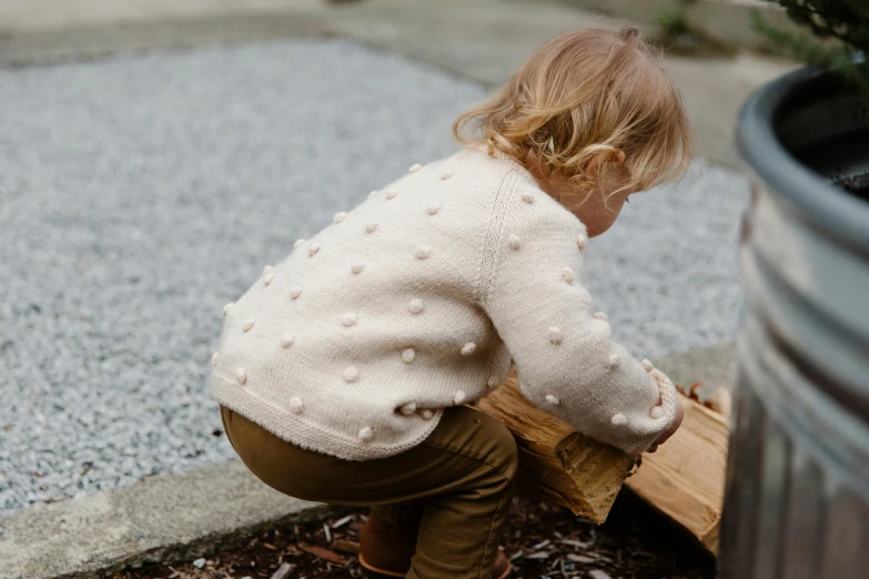 a small child playing with a piece of wood, inspired by Elsa Beskow, unsplash, wearing a cardigan, varying dots, knees upturned, highly detailled texture