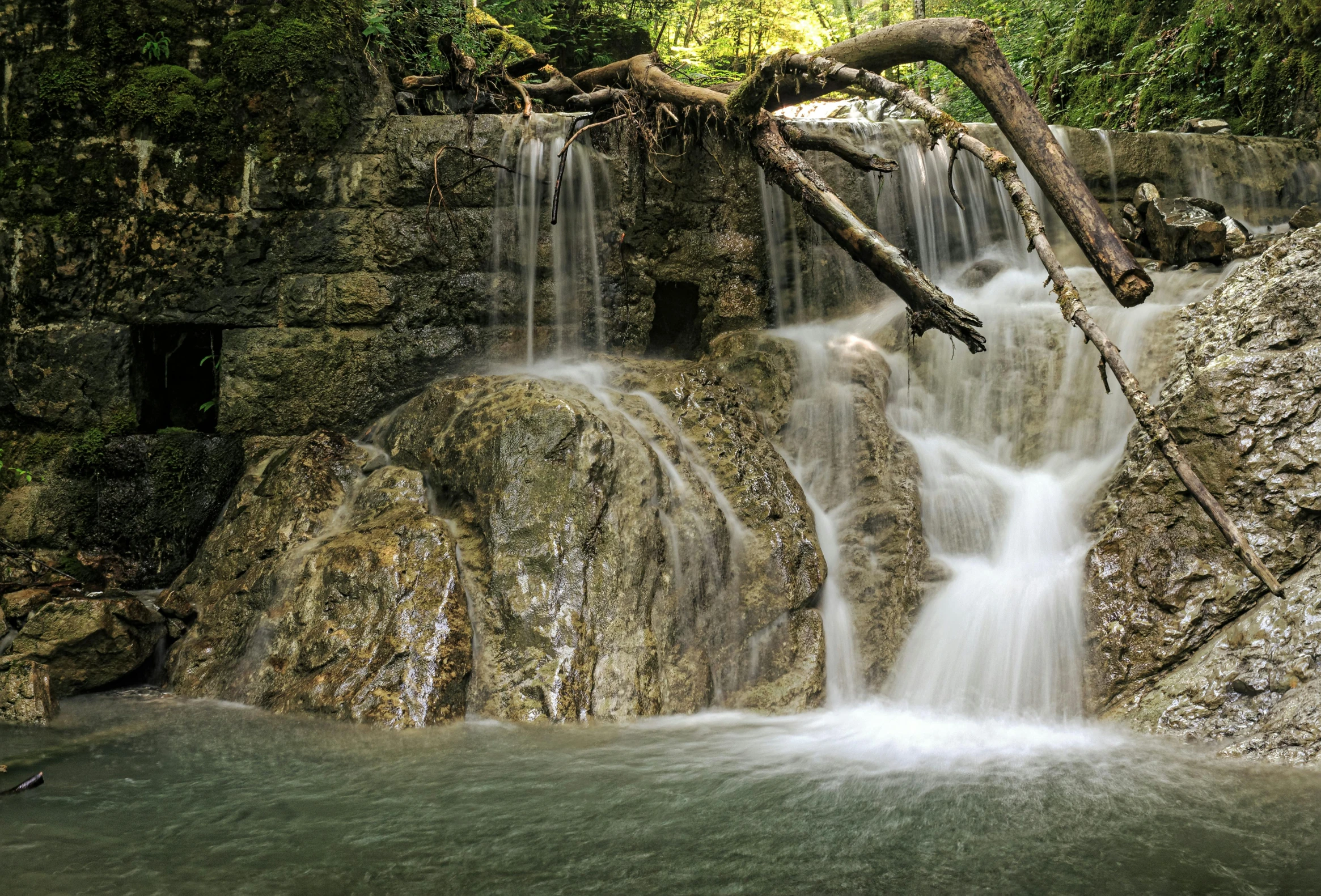 a waterfall in the middle of a lush green forest, by Mirko Rački, pexels contest winner, hurufiyya, water flowing through the sewer, panoramic, brown, grotto