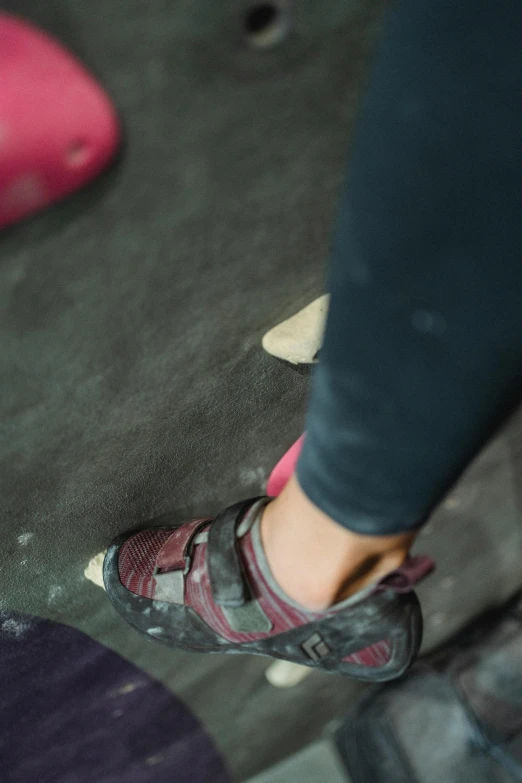 a person standing on a rock climbing wall, pink shoes, up close image, sitting on the floor, f/1.4