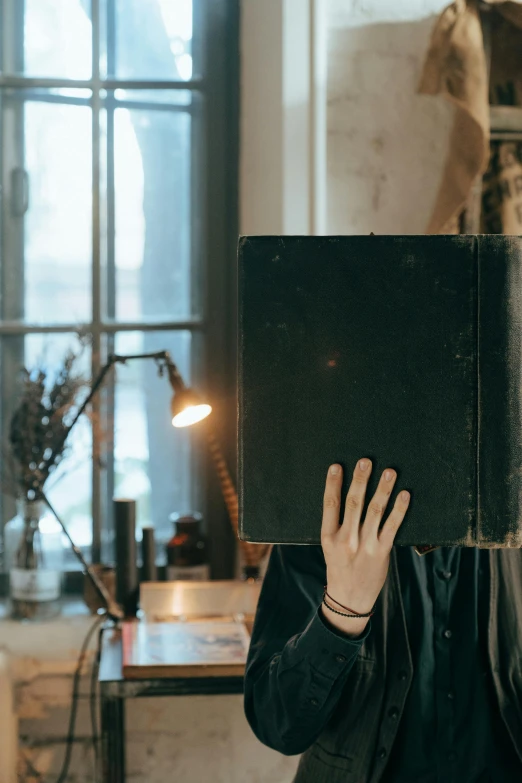 a woman holding a book in front of her face, an album cover, pexels contest winner, emerging from her lamp, he is holding a large book, dark university aesthetic, working in an office