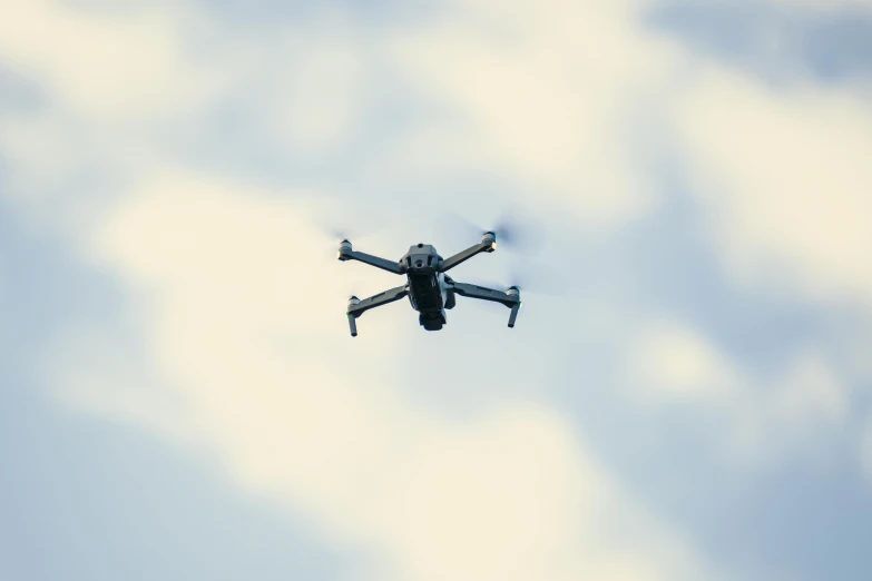 a black drone flying through a cloudy blue sky, by Carey Morris, pexels, hurufiyya, police drones, holiday season, b - roll, a green