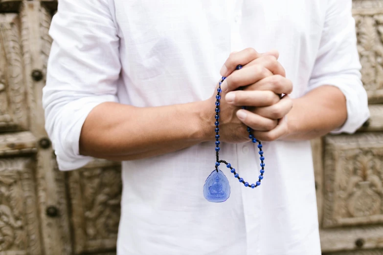 a close up of a person holding a rosary, unsplash, hurufiyya, blue translucent resin, asian male, wearing greek palla, official product photo