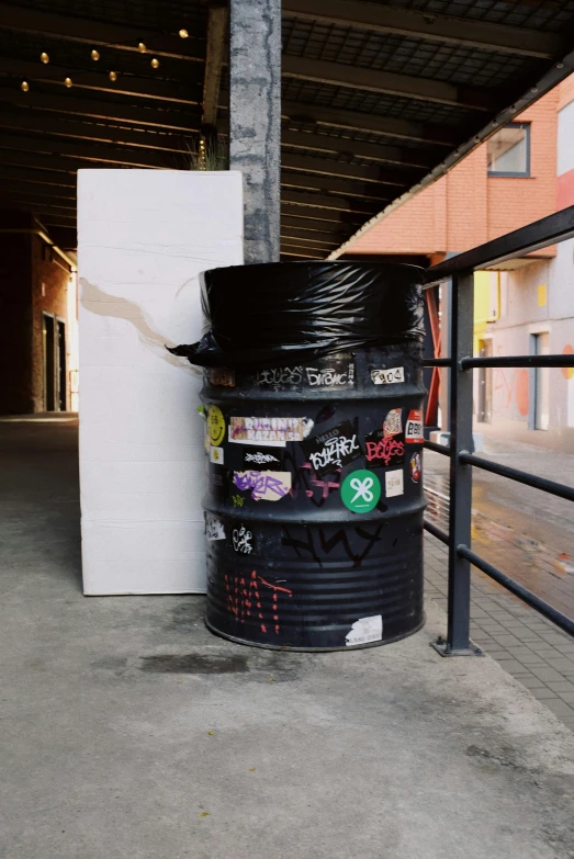 a trash can sitting next to a metal fence, an album cover, unsplash, graffiti, in a warehouse, stickers, huge black circle, stacked