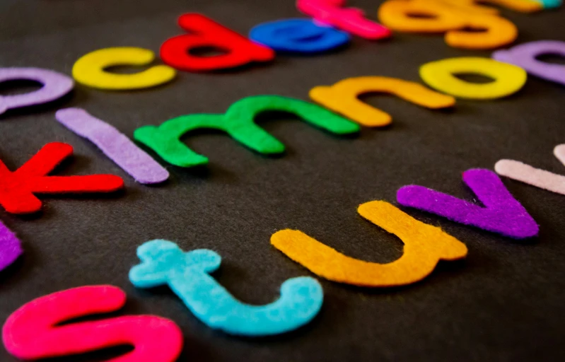 a close up of colorful wooden letters on a black surface, pexels, needle felting, fan favorite, blackboard, teaching