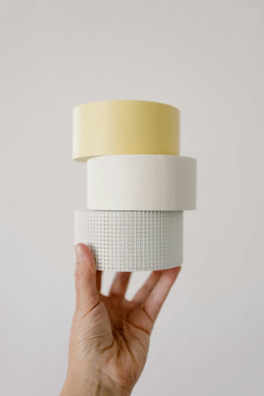 a person holding a stack of tape in their hand, light cream and white colors, porcelain forcefield, 3 colours, cardstock