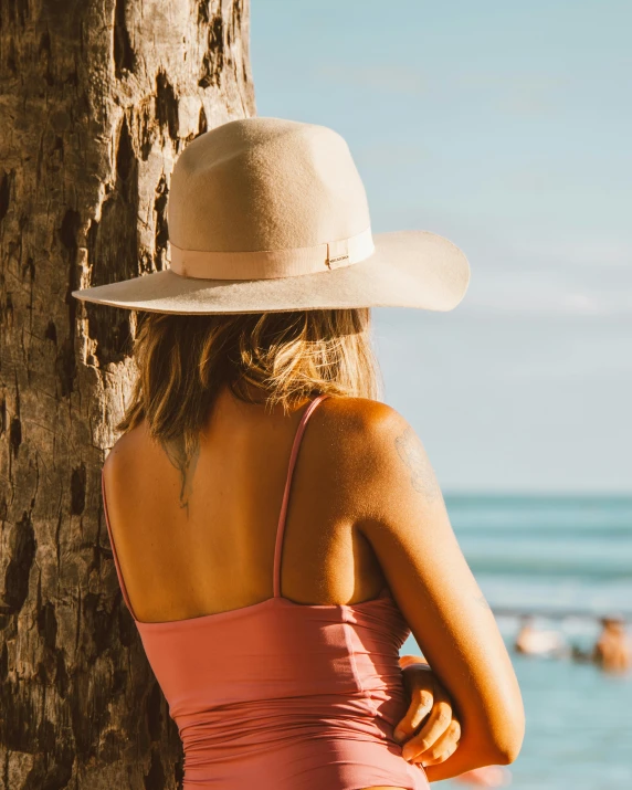 a woman standing next to a tree on a beach, by Maggie Hamilton, trending on pexels, pink cowboy hat, tanned body, profile image, sitting on a bench