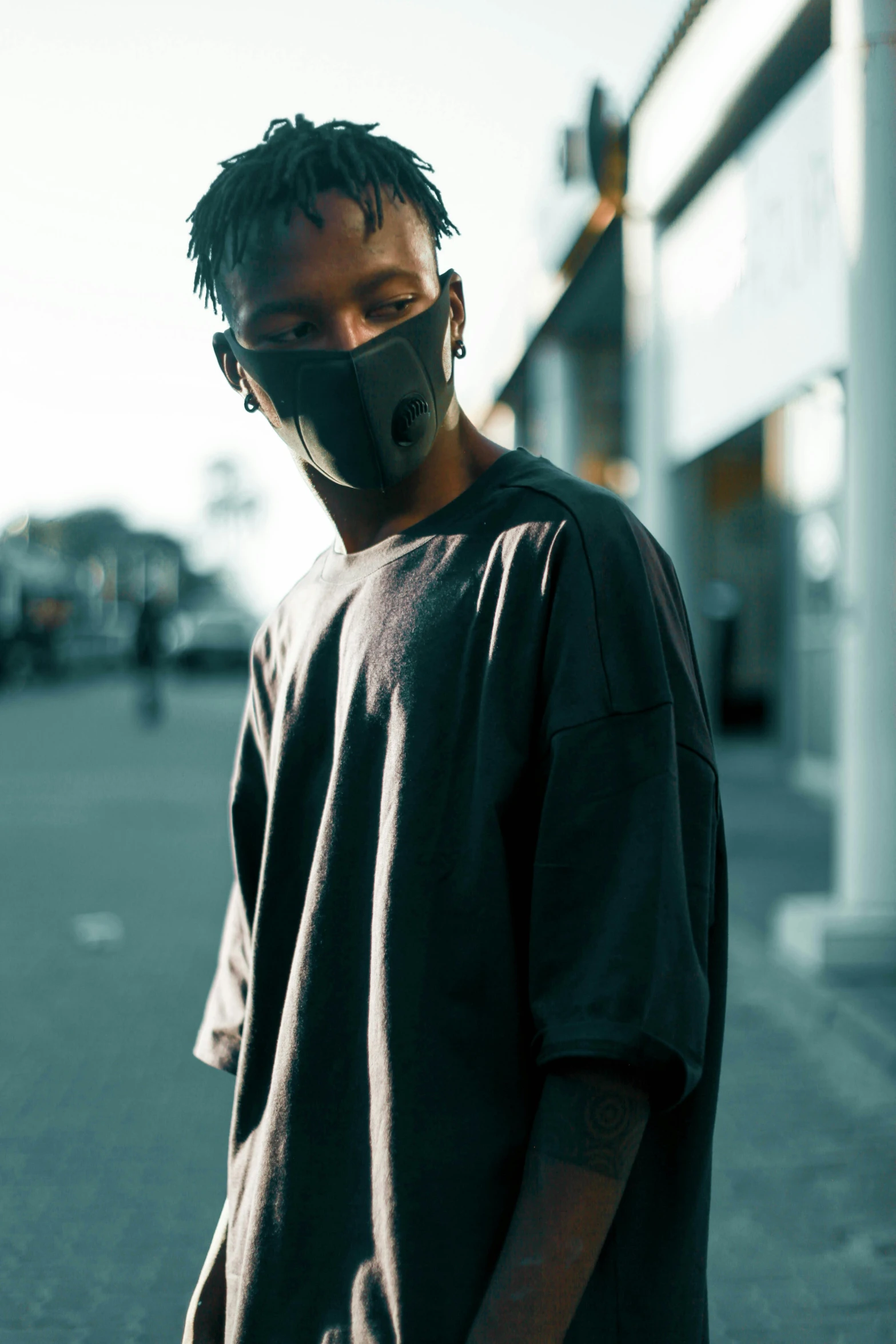 a man wearing a face mask standing in a parking lot, an album cover, by Bascove, unsplash, techwear clothes, portrait willow smith, profile image, wide neck