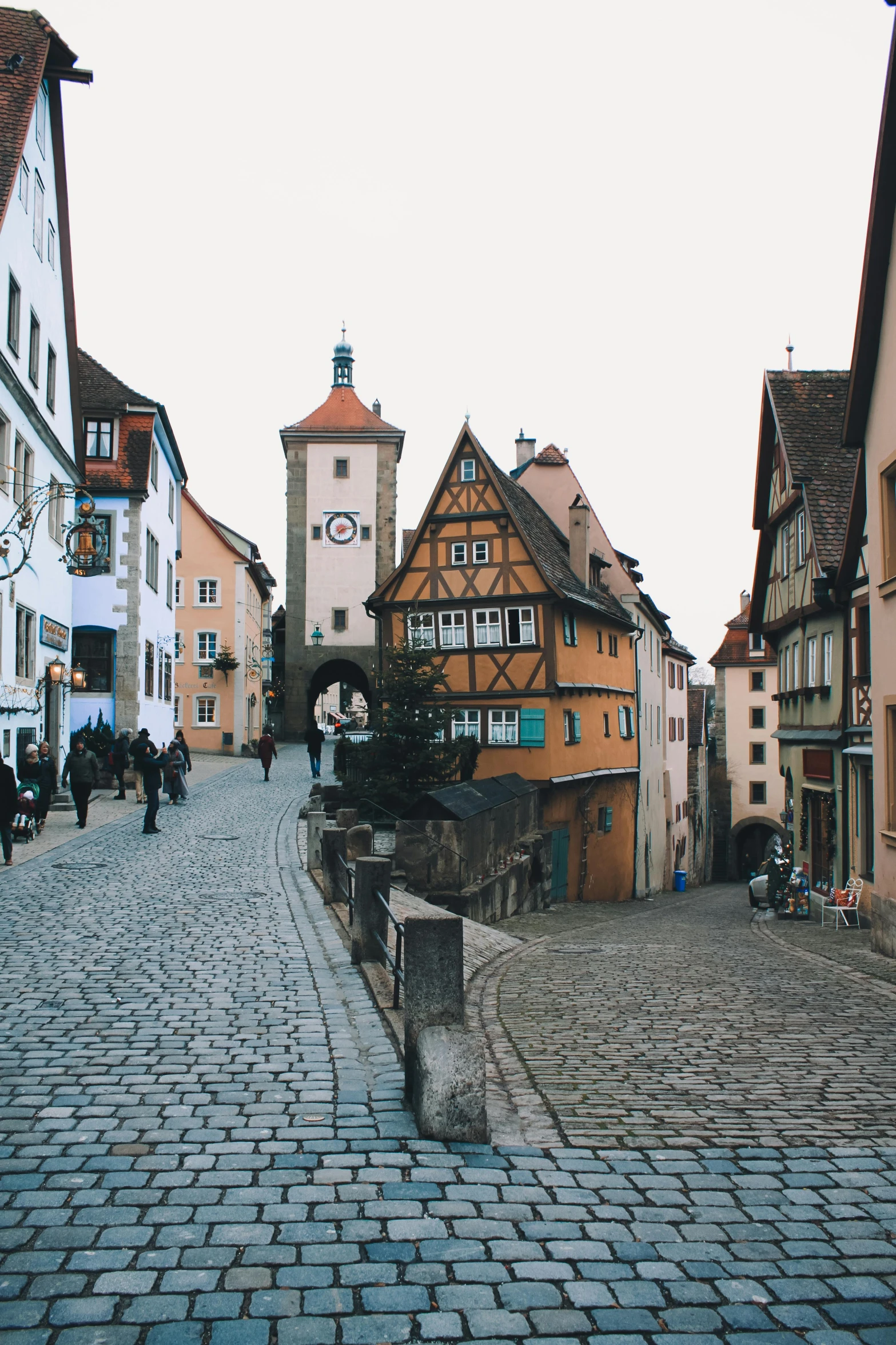 a cobblestone street with a clock tower in the background, an album cover, by Jacob Burck, trending on unsplash, renaissance, alpine architecture, german renaissance architecture, pilgrim village setting, square