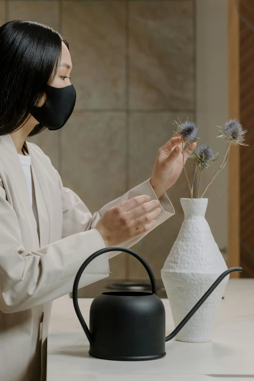 a woman wearing a face mask watering flowers, inspired by Kanō Naizen, hand on table, oled visor for eyes, black, porcelain