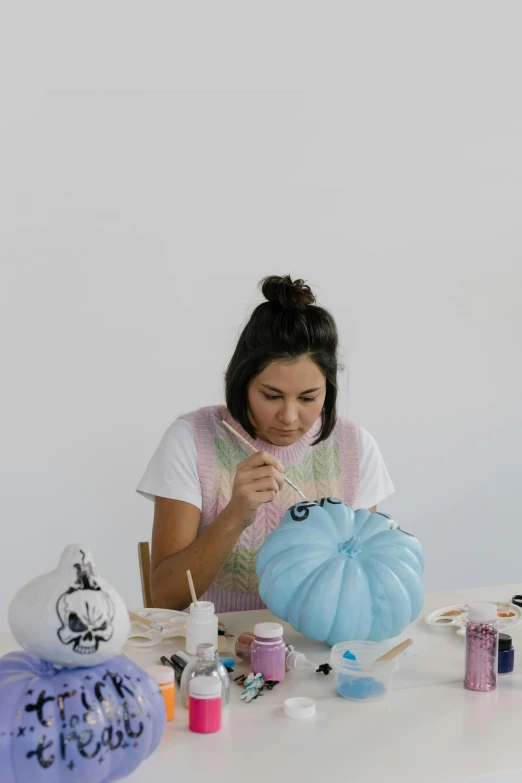 a woman sitting at a table painting a blue pumpkin, jen atkin, cast, fernanda suarez, pose 4 of 1 6