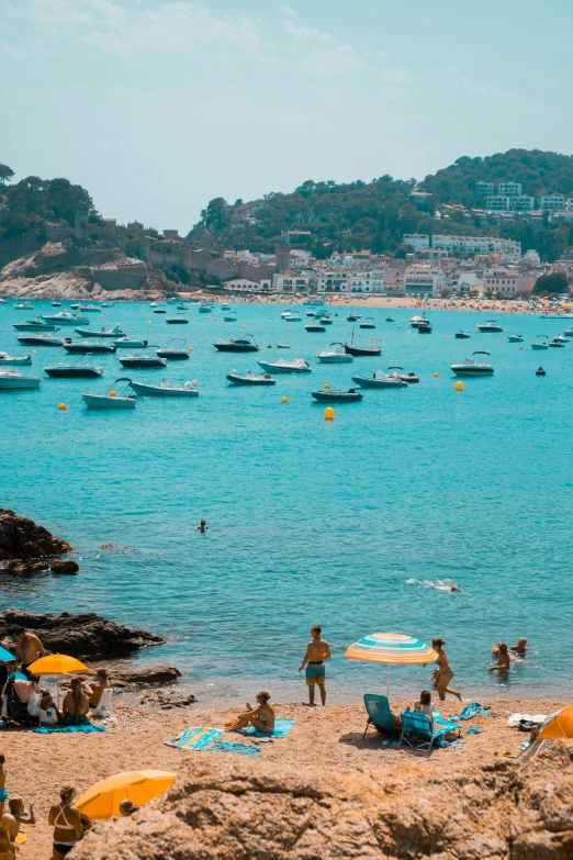 a group of people sitting on top of a sandy beach, boats in the water, in spain, sparkling cove, square