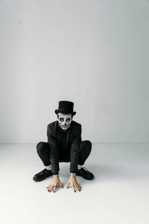 a man in a black suit and top hat sitting on the floor, inspired by James Bolivar Manson, pexels contest winner, neo-dada, mime, skull mask, in a white room, concert