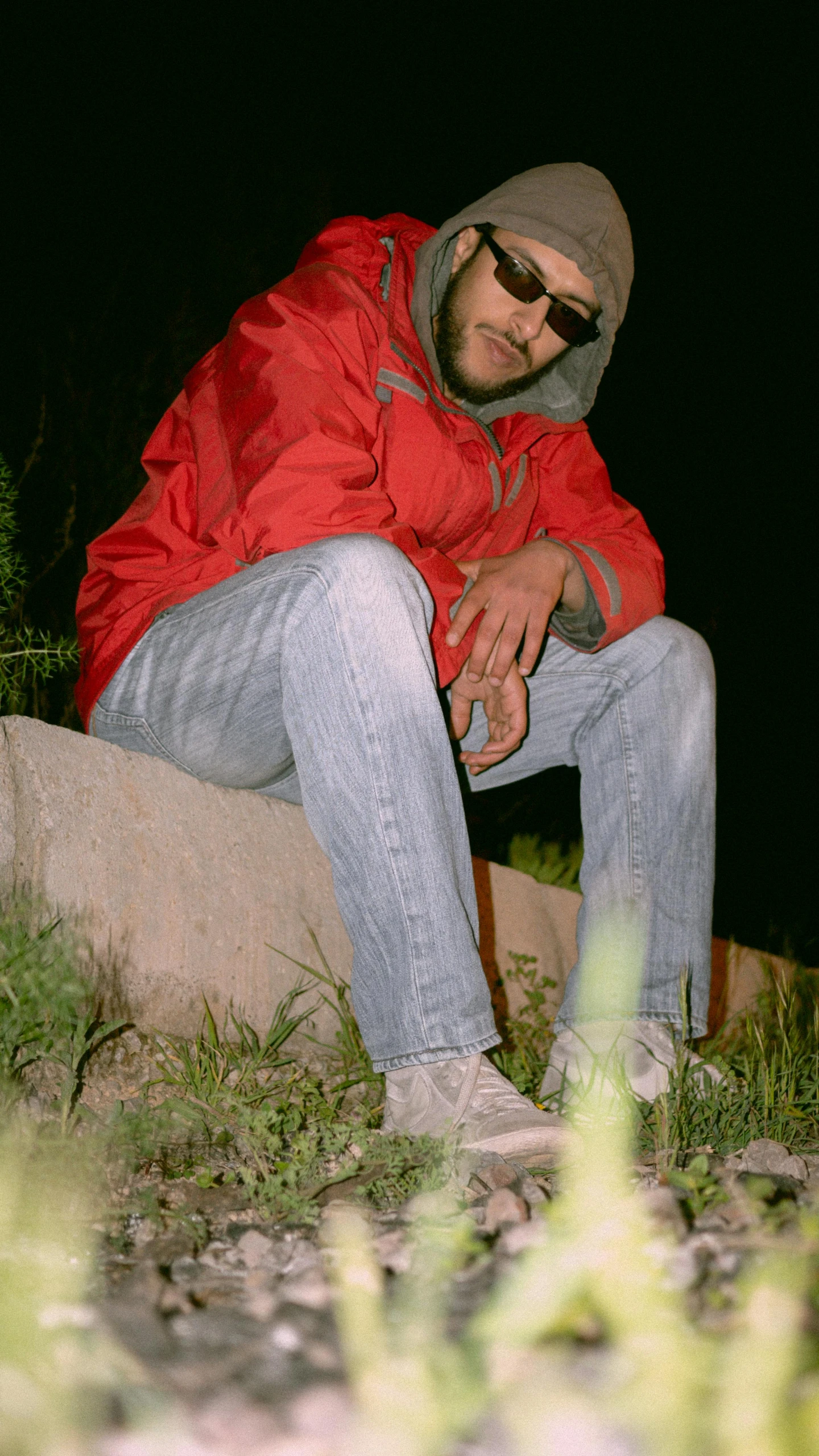 a man in a red jacket sitting on a rock, an album cover, unsplash, hurufiyya, low quality photo, scanned, ((((((((night)))))))) day time, doing a sassy pose