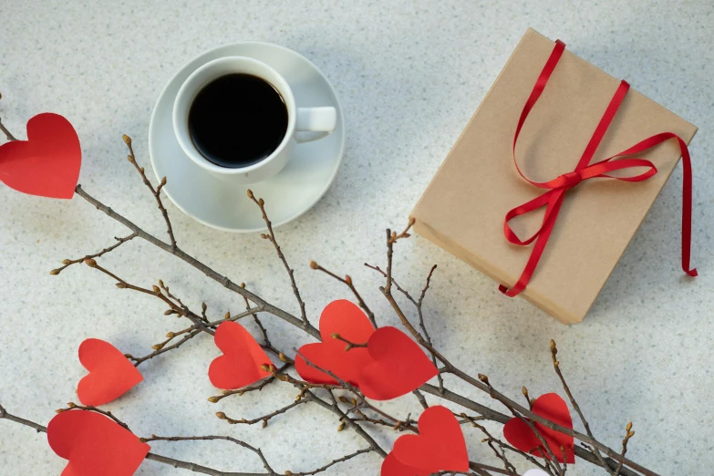 a cup of coffee sitting on top of a table, by Valentine Hugo, pexels contest winner, romanticism, holding gift, paper decoration, red hearts, product shot