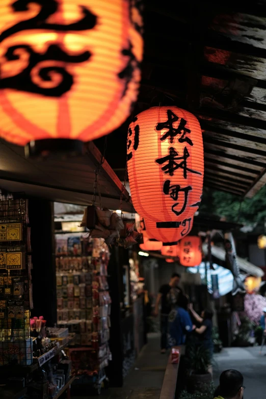 a group of lanterns hanging from the side of a building, a picture, reddit, mingei, glowing street signs, market setting, oriental scene, with orange street lights