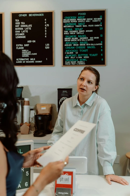 a couple of people that are sitting at a table, at checkout, emily rajtkowski, centered shot, talking