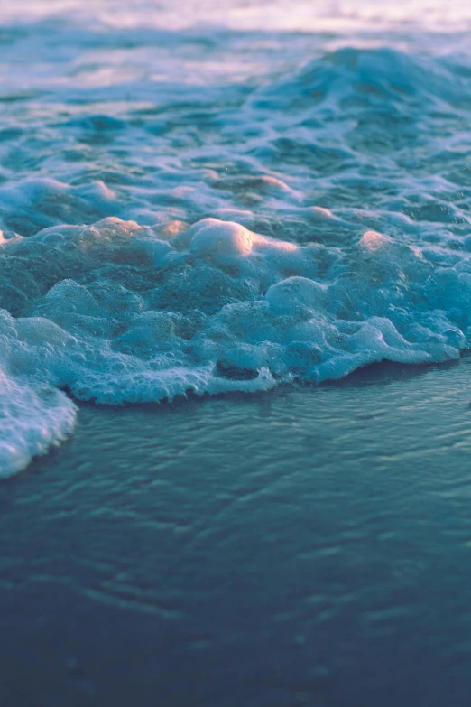 a surfboard sitting on top of a beach next to the ocean, an album cover, inspired by Elsa Bleda, unsplash, water ripples, sea foam, a close-up, glowing water with caustics