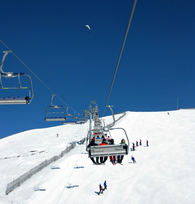 a group of people riding a ski lift down a snow covered slope, les nabis, light blue clear sky, blue clear skies, item, a wooden