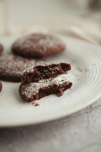 a white plate topped with chocolate cookies next to a glass of milk, powdered sugar, close - up profile, alessio albi, detailed product image