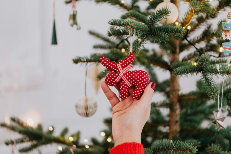 a person holding a christmas ornament in front of a christmas tree, by Julia Pishtar, pexels, folk art, rabbit ears, polka dot, cosy, soft grey and red natural light