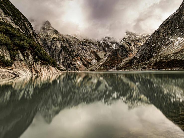 a body of water surrounded by mountains under a cloudy sky, by Peter Churcher, pexels contest winner, hyperrealism, symmetrical image, lpoty, craggy, belgium