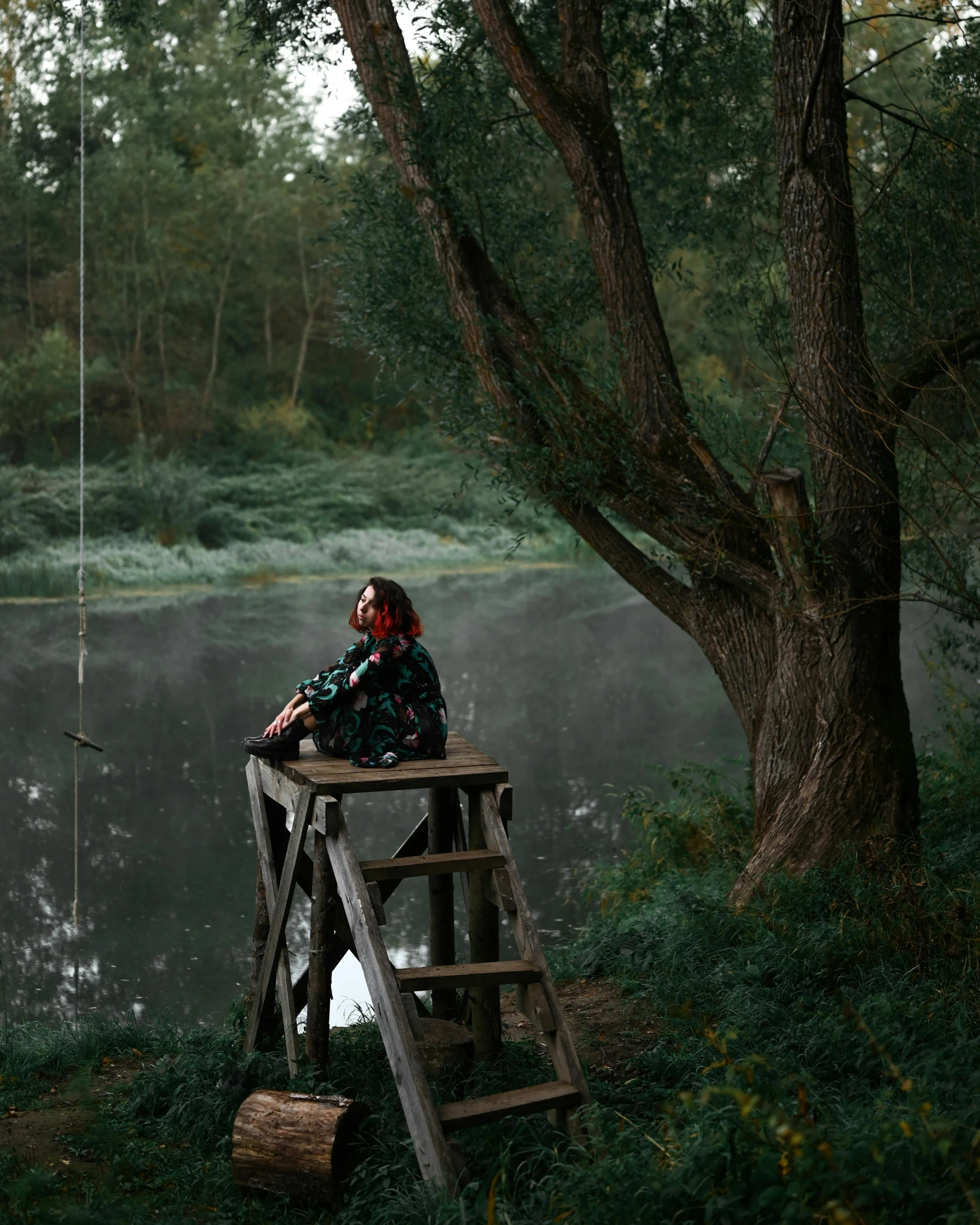 a man sitting on top of a wooden platform next to a body of water, inspired by Elsa Bleda, pexels contest winner, romanticism, perched in a tree, photo of the girl, ukraine. photography, multiple stories