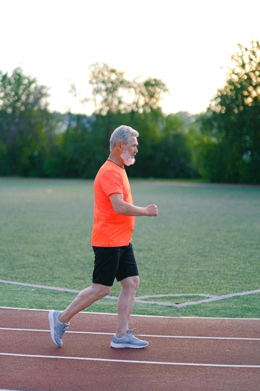 a man in an orange shirt is running on a track, old gigachad with grey beard, profile image, on a soccer field, wearing fitness gear