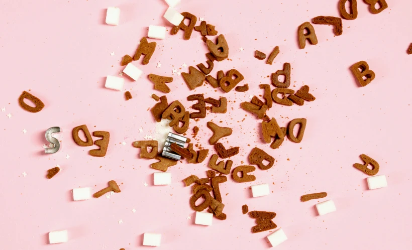 a pile of chocolate letters sitting on top of a pink surface, a jigsaw puzzle, by Julia Pishtar, milkshake, thumbnail, damaged, product shot