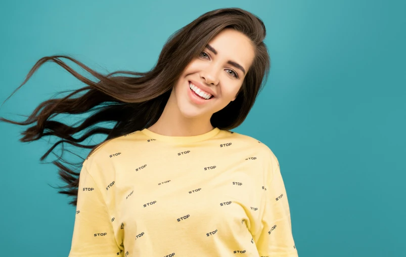 a woman with long hair standing in front of a blue background, trending on pexels, pop art, wearing a modern yellow tshirt, repeating pattern, smileing nright, wearing sweatshirt