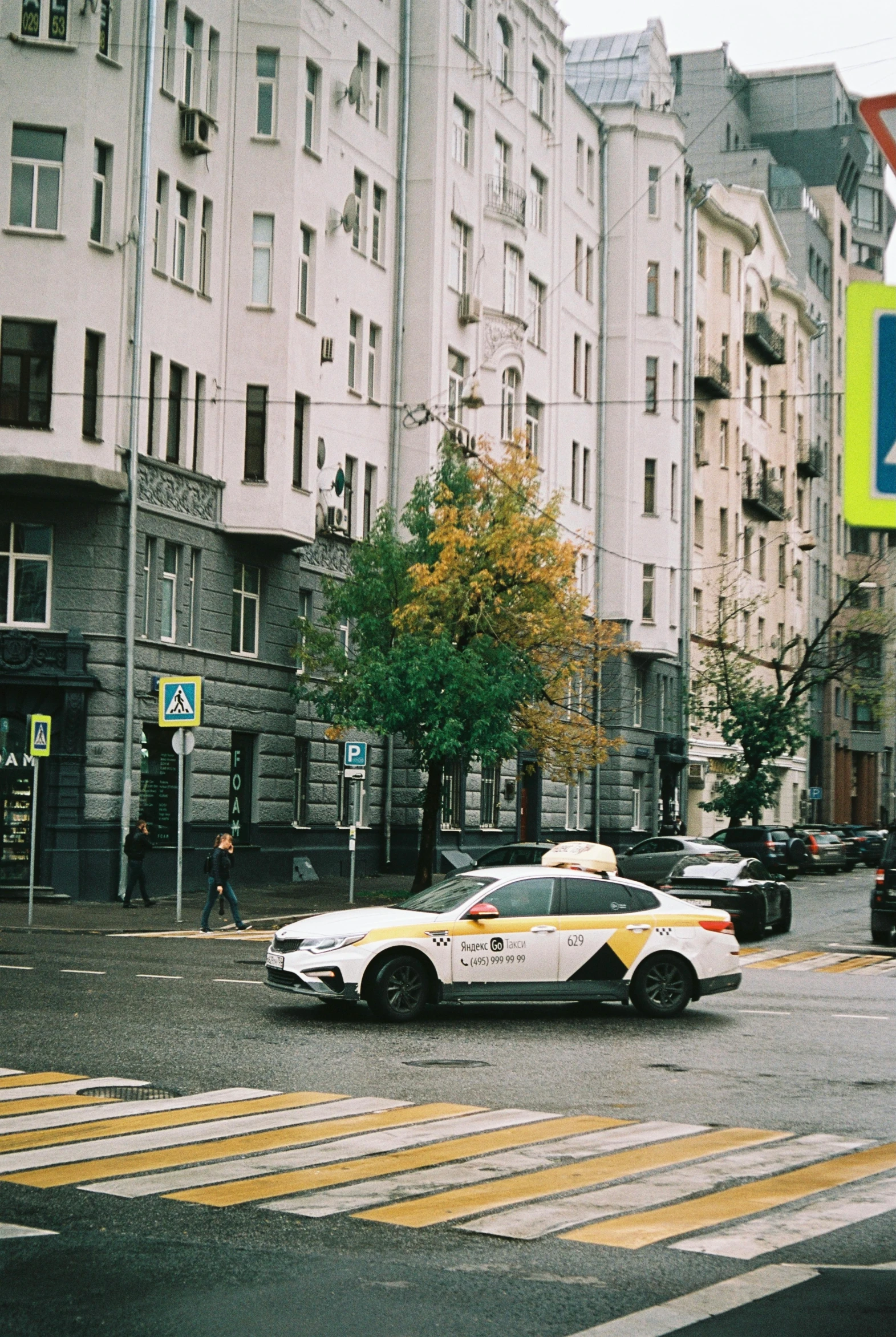 a yellow taxi driving down a street next to tall buildings, an album cover, inspired by Pavel Fedotov, 000 — википедия, police station, leica s photograph, gif