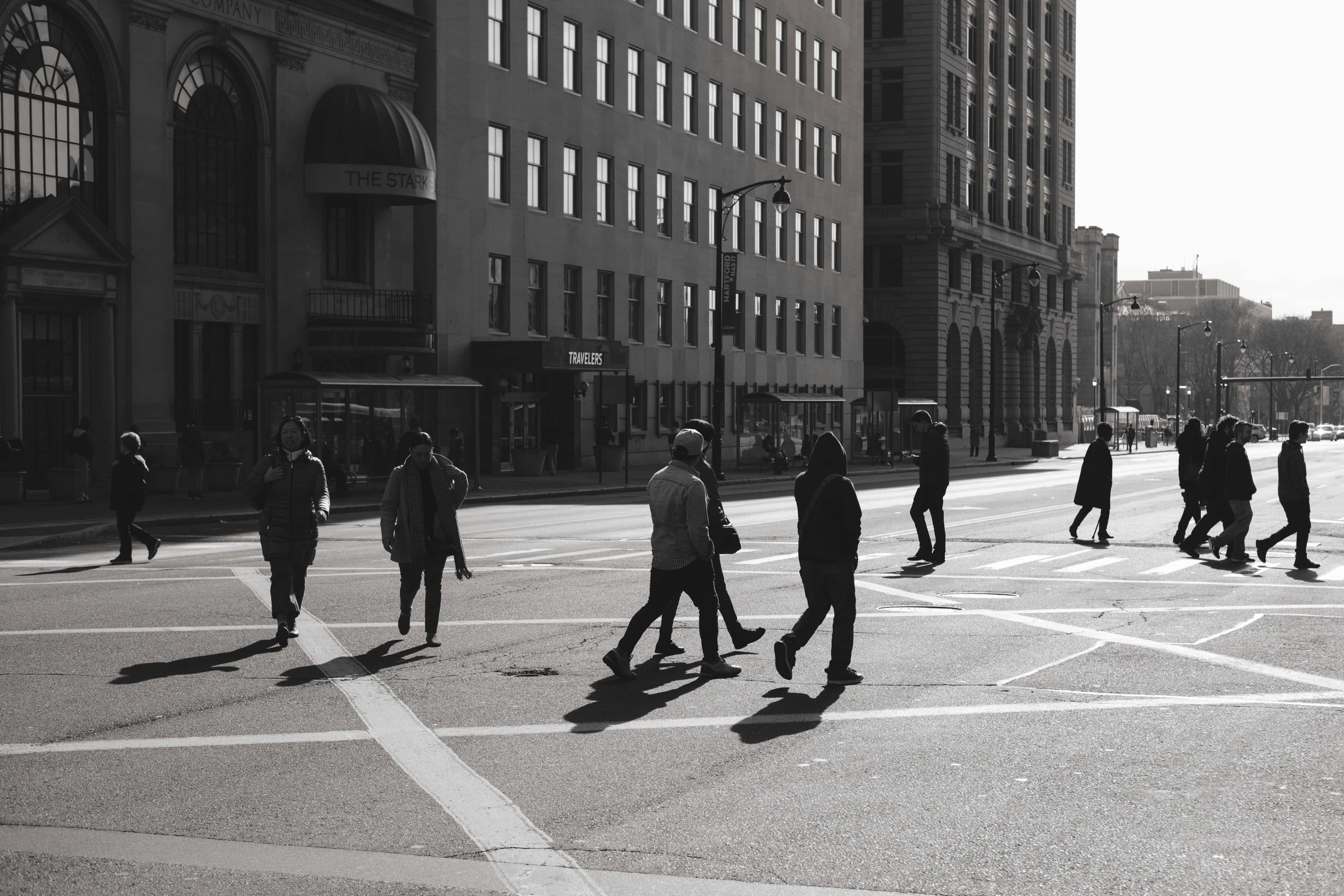 a group of people walking across a street, a black and white photo, pexels contest winner, full morning sun, downtown, shadow gradient, instagram post