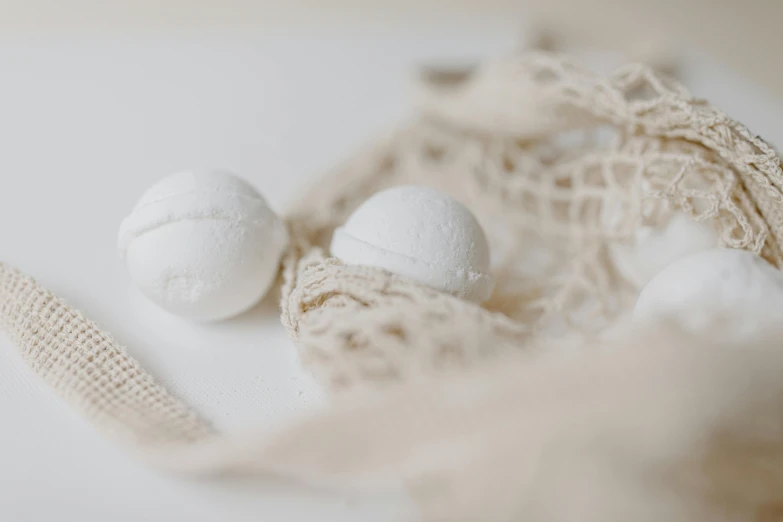 a bag of bath bombs sitting on top of a table, by Emma Andijewska, unsplash, baroque, dressed in white intricate lace, matte white background, spheres, nets