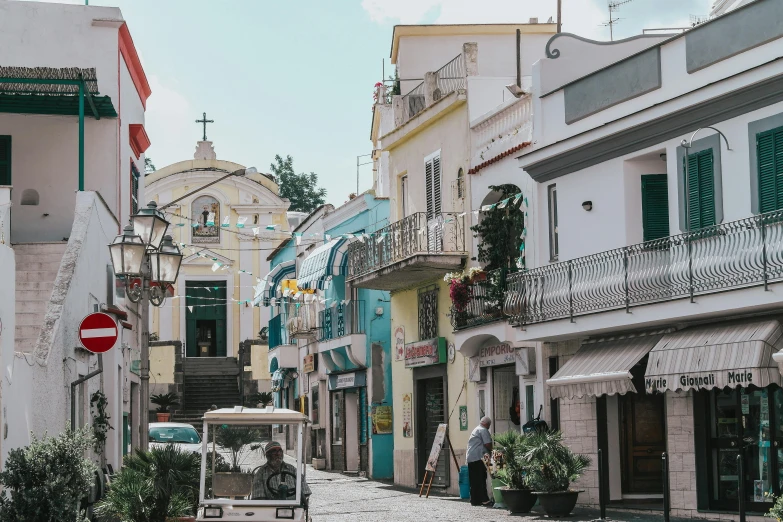 a couple of people walking down a cobblestone street, pexels contest winner, renaissance, capri coast, driving through a 1 9 5 0 s town, house's and shops and buildings, tropical coastal city