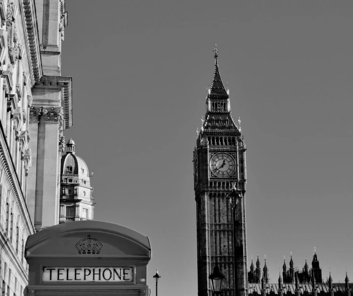 a telephone booth with a clock tower in the background, a black and white photo, by Robin Guthrie, pixabay, the houses of parliament, blue sky, square, brutalist buildings tower over