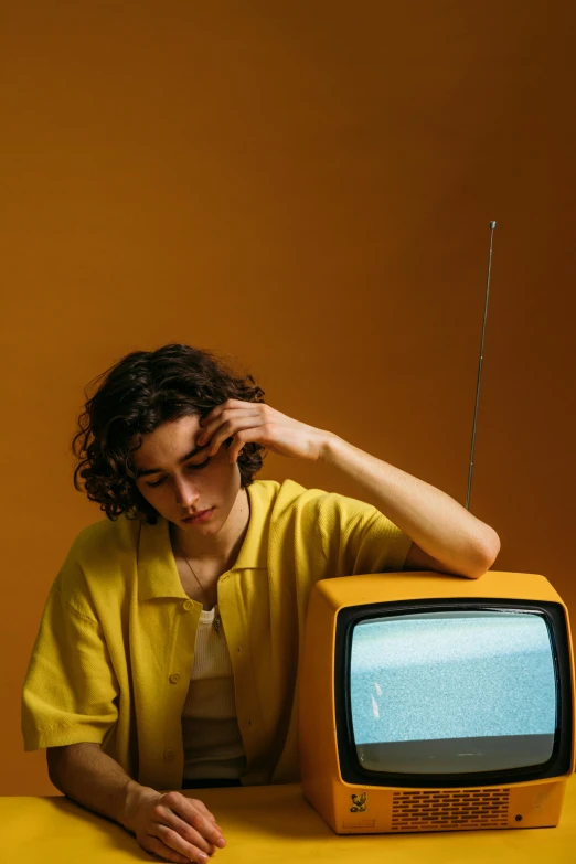 a man sitting at a table with a television in front of him, inspired by Elsa Bleda, trending on pexels, magic realism, wavy hair yellow theme, teenage girl, studio shoot, rebecca sugar