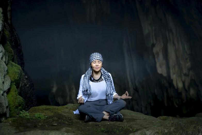 a woman sitting in a meditation position on a rock, an album cover, inspired by Li Di, hurufiyya, cave exploration, vietnam, 2019 trending photo, islamic