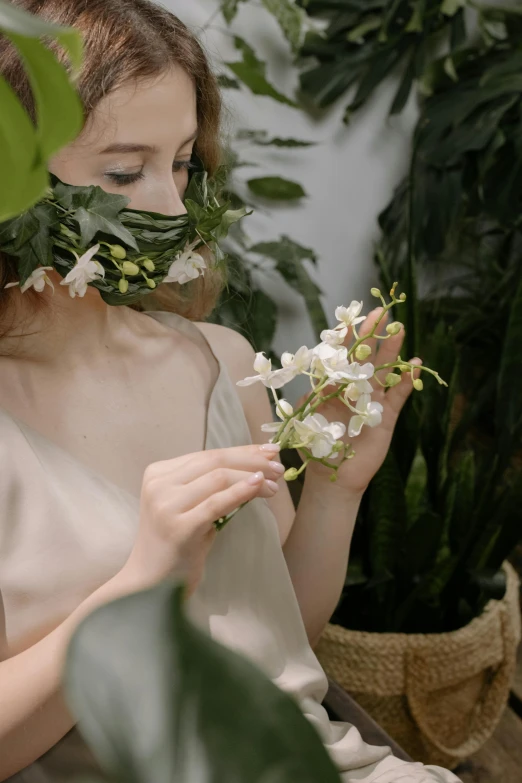 a woman holding a flower in front of her face, inspired by Konstantin Somov, trending on unsplash, white orchids, soft silk dress, with ivy, video still