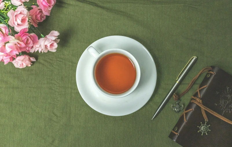 a cup of tea and a notebook on a table, inspired by Charles Le Roux, trending on pexels, arts and crafts movement, green and pink fabric, chopsticks, striking pose, botanicals