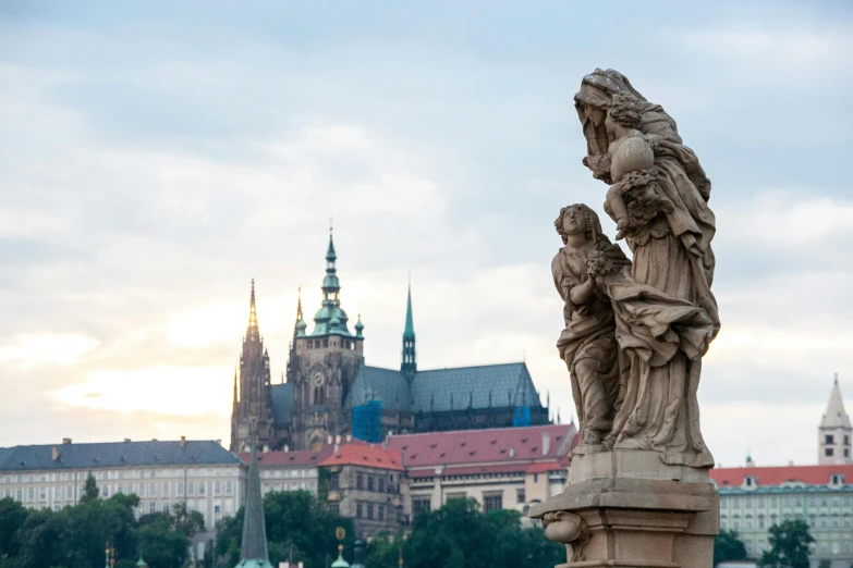 a statue of a woman holding a child with a castle in the background, a statue, by Matija Jama, pexels contest winner, art nouveau, majestic spires, early evening, tall bridge with city on top, statue of carving marble