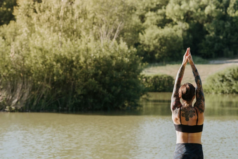 a woman doing yoga in front of a body of water, unsplash, process art, sydney park, near pond, arms out, detailed surroundings