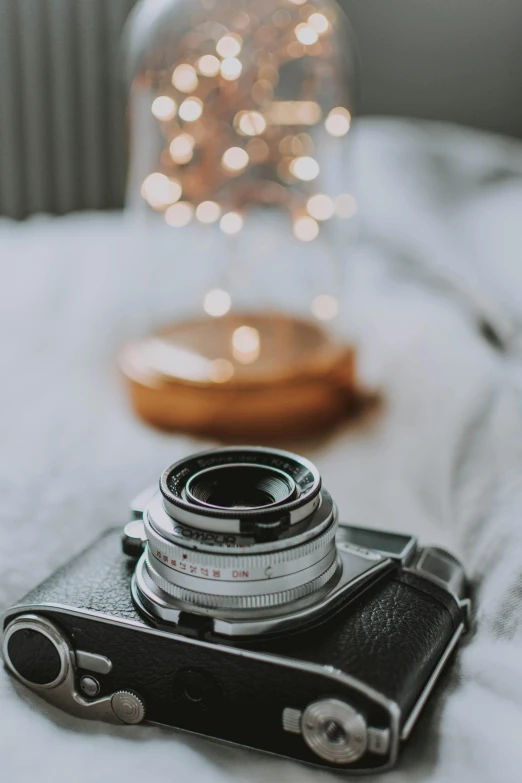 a camera sitting on top of a bed next to a lamp, unsplash contest winner, hasselblad film bokeh, holiday, on a white table, vintage camera