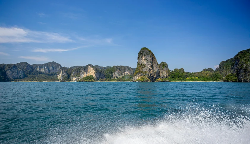 a large body of water with mountains in the background, a picture, thailand, large waves hitting the cliff, on a boat, slide show