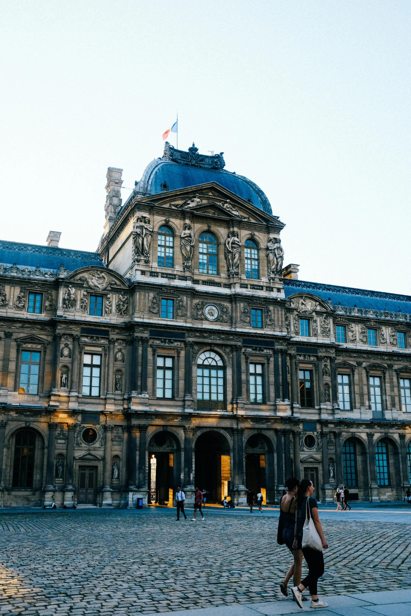 two people walking in front of a large building, inspired by Jean-François de Troy, trending on unsplash, paris school, on display in the louvre, square, summer evening, exterior wide shot