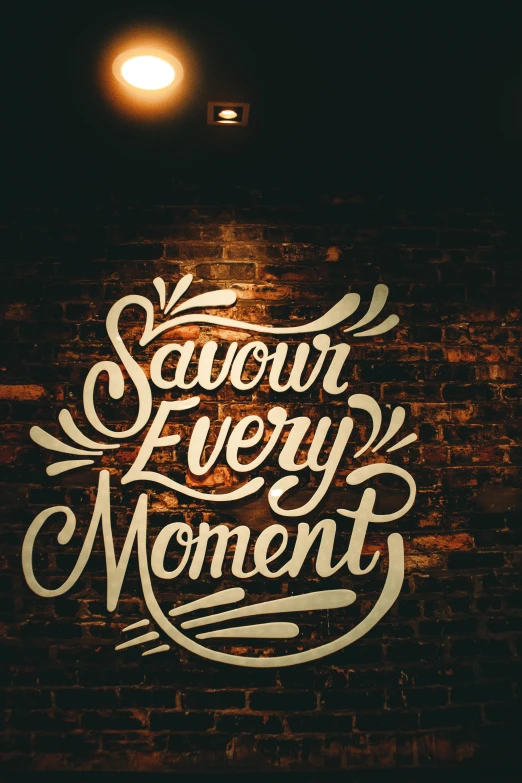 a brick wall with a sign that says savor every moment, inspired by Jacob Savery, pexels contest winner, graffiti, saturday night in a saloon, cosy atmosphere, thumbnail, profile picture