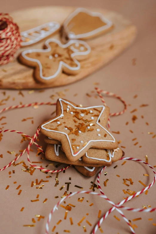 a couple of cookies sitting on top of a wooden cutting board, by Julia Pishtar, glittering stars scattered about, with ornamental edges, ginger, ribbon